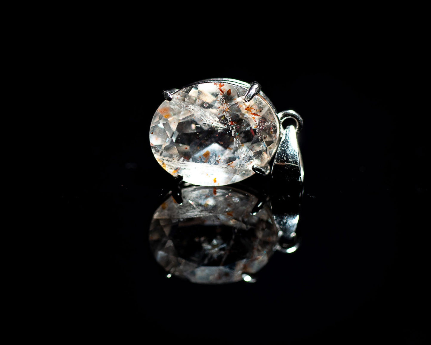 A pendant with a large, orange confetti sunstone set in a silver mounting, displayed against a black background.