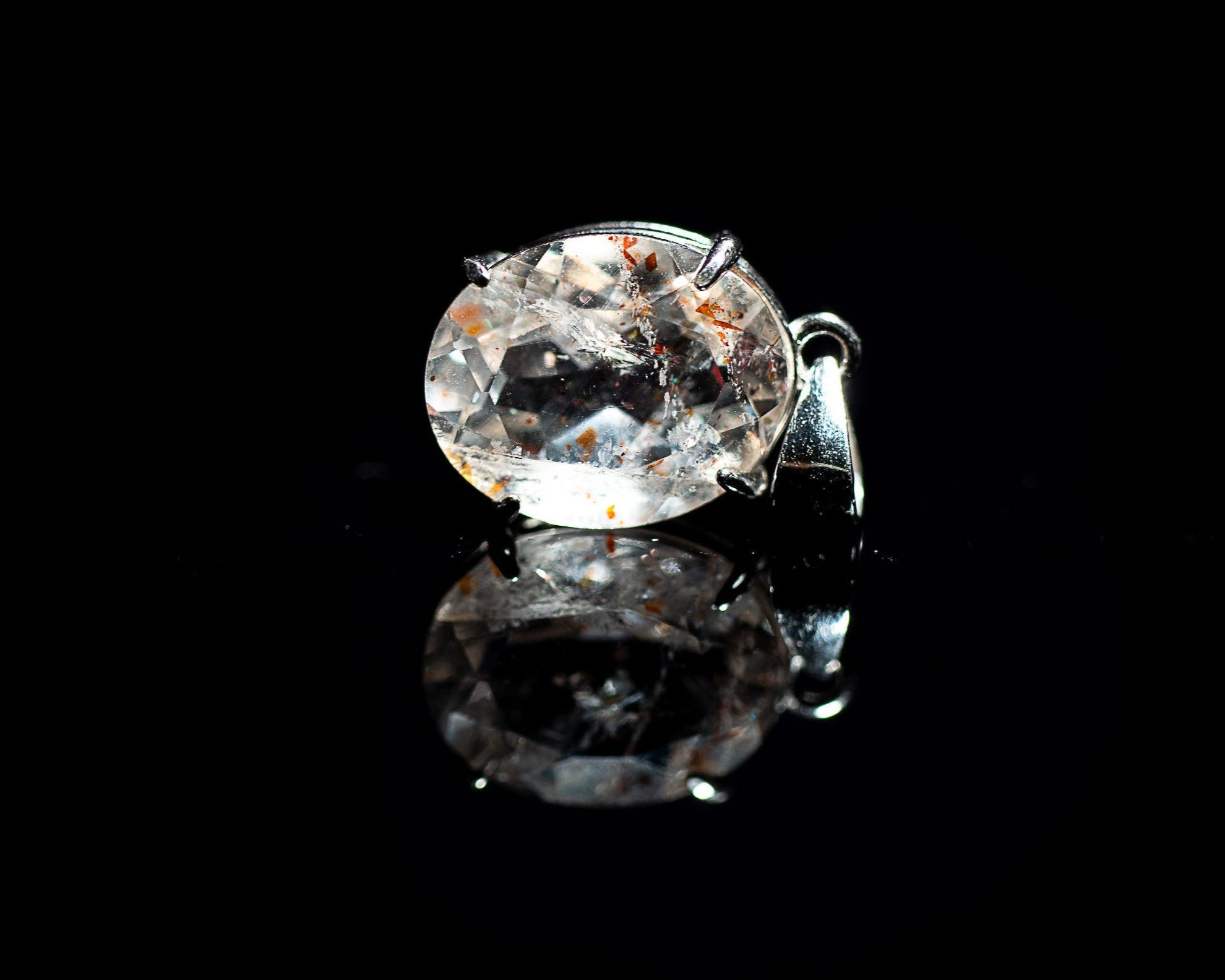 A pendant with a large, orange confetti sunstone set in a silver mounting, displayed against a black background.